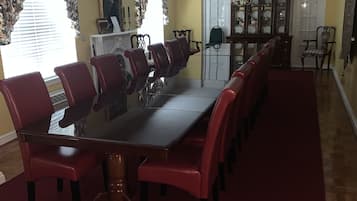 A dining area with a long table and red chairs, a wooden cabinet, and a patterned curtain.