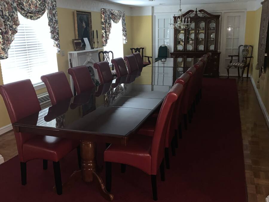 A dining area with a long table and red chairs, a wooden cabinet, and a patterned curtain.