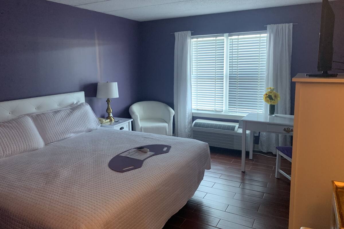 A hotel room with a large bed, a desk, a chair, and a window with blinds.