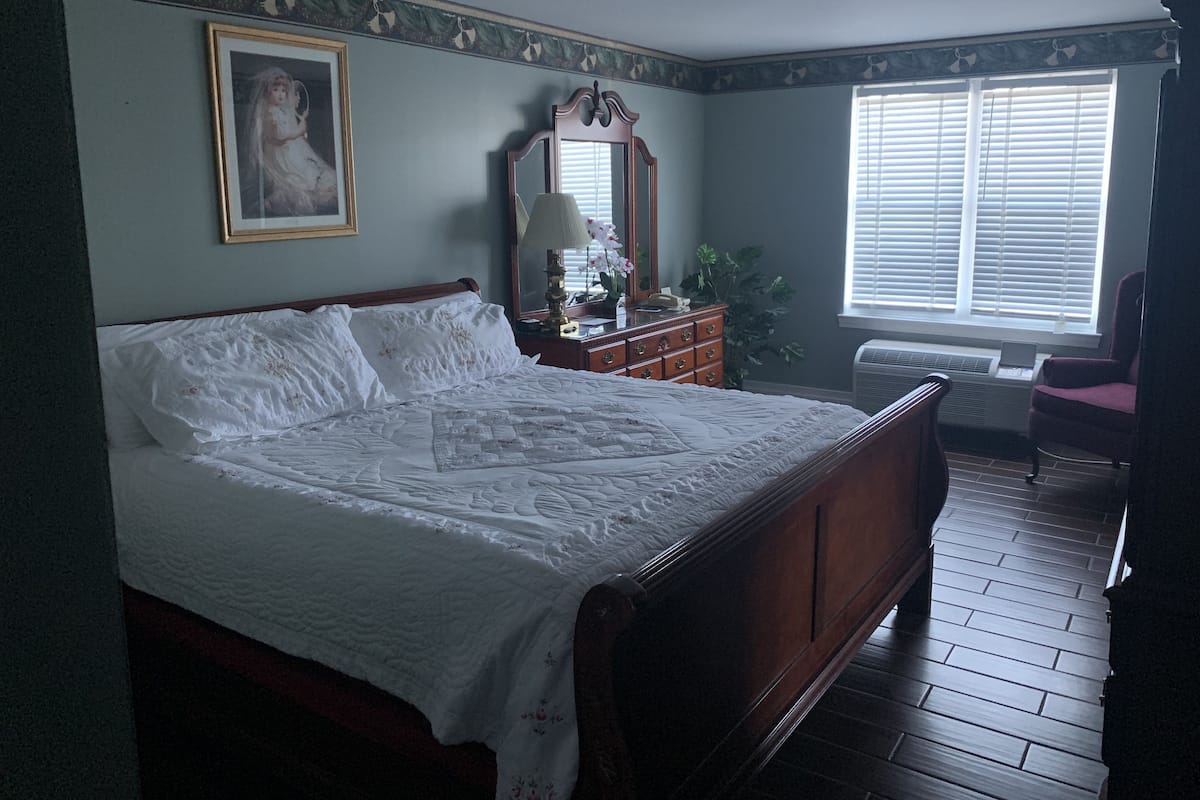 A bedroom with a large bed, a dresser, a mirror, and a window with blinds.