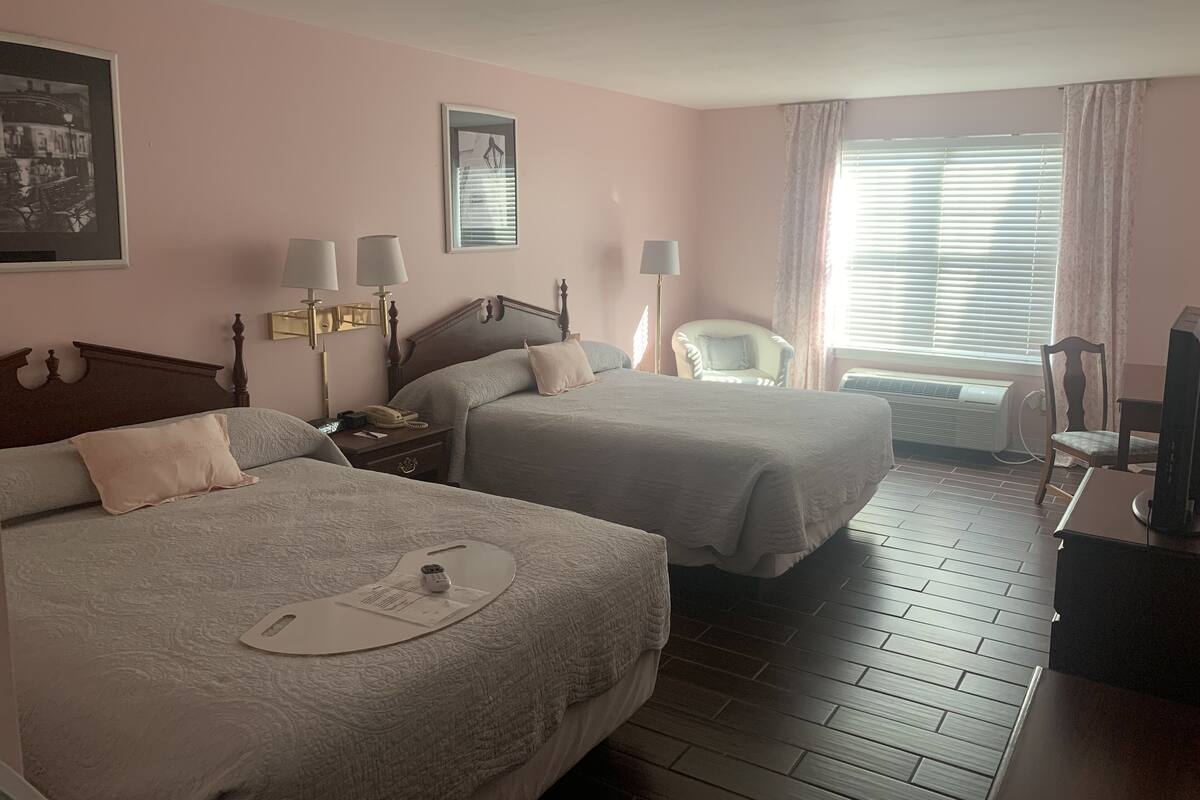 A hotel room with two beds, a chair, a desk, and a window with blinds.