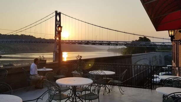 Ein Außenbereich mit Tischen und Stühlen mit Blick auf einen Fluss und eine Brücke.