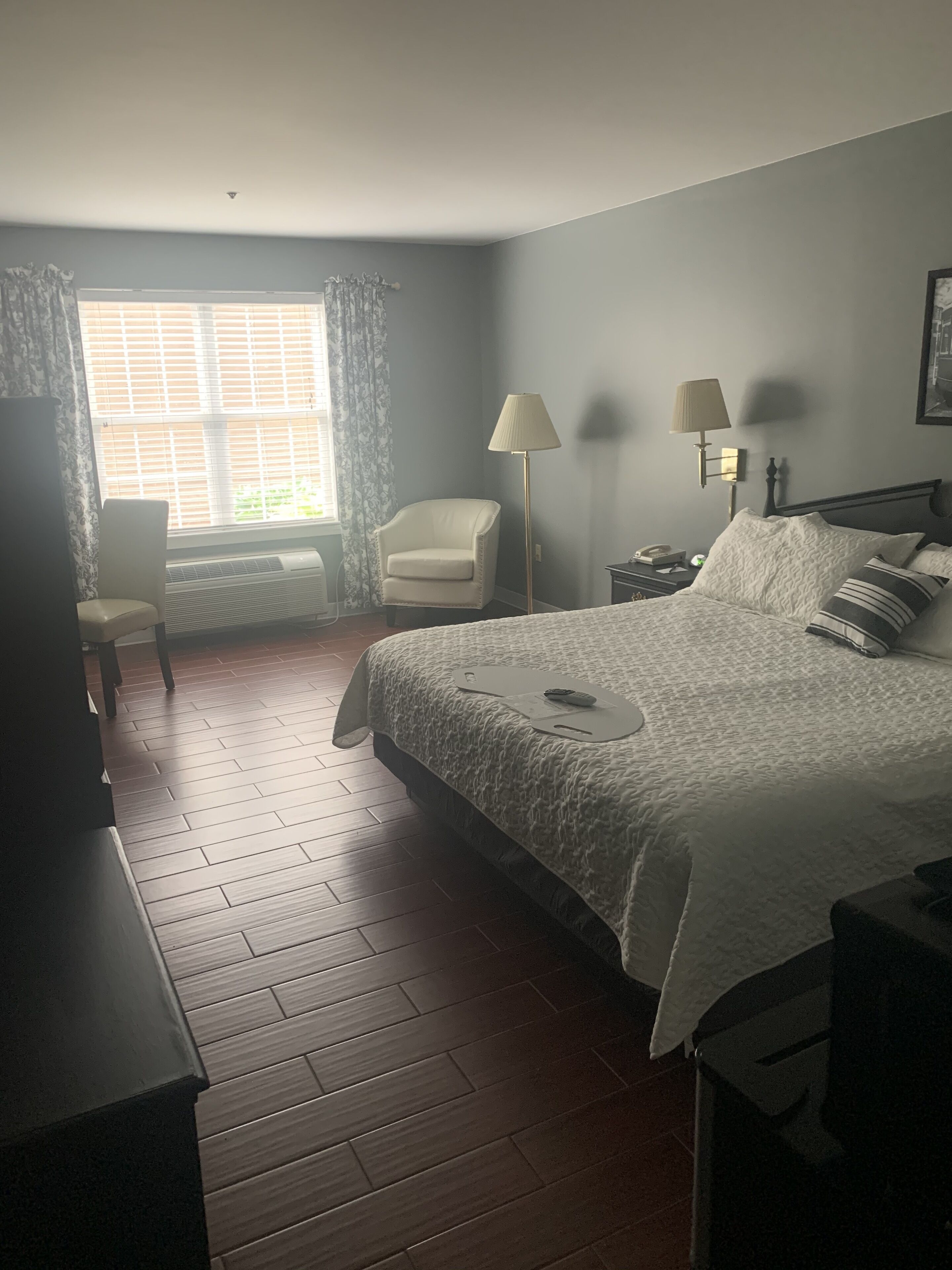 Un dormitorio con cama, una silla, un escritorio, una lámpara y una ventana con cortinas.