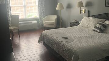 Un dormitorio con cama, una silla, un escritorio, una lámpara y una ventana con cortinas.