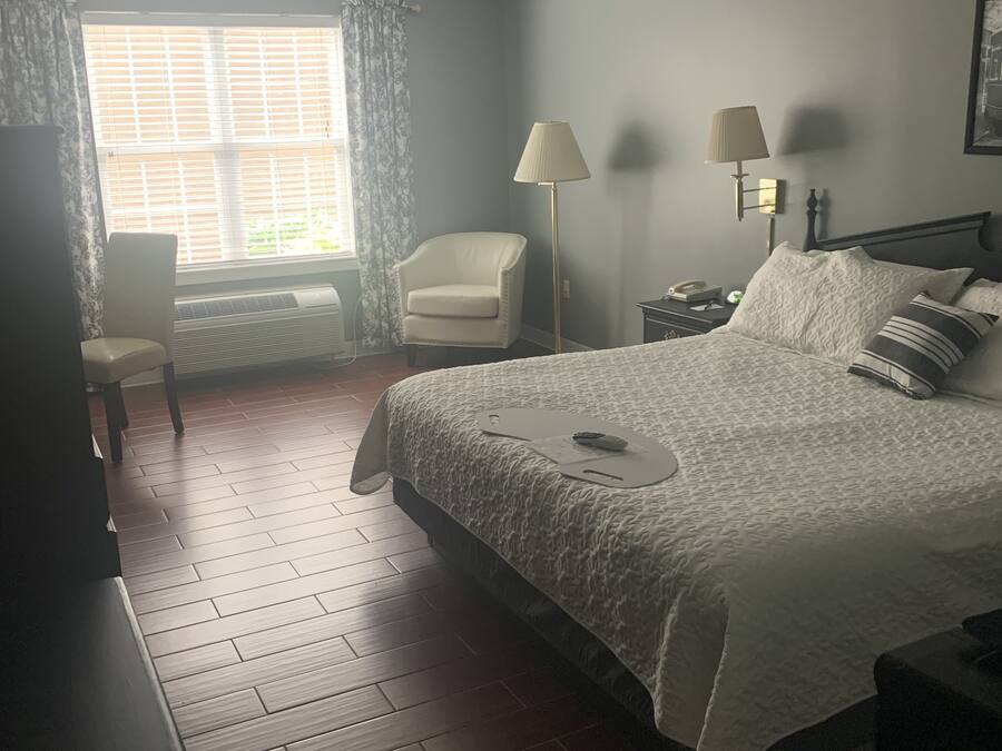 Un dormitorio con cama, una silla, un escritorio, una lámpara y una ventana con cortinas.