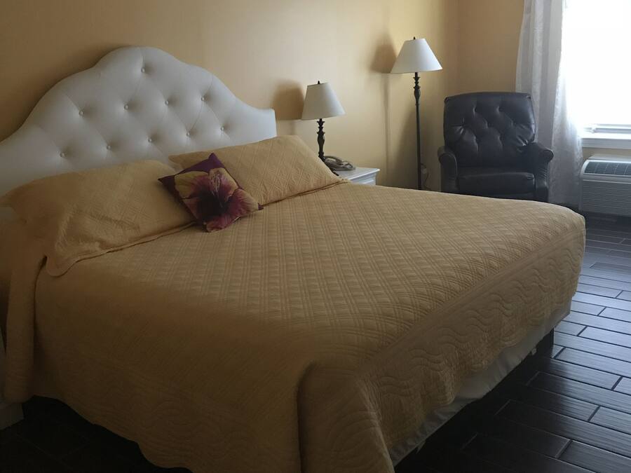 Una habitación de hotel con una cama grande, dos lámparas de noche, una silla y un ventanal con cortinas.