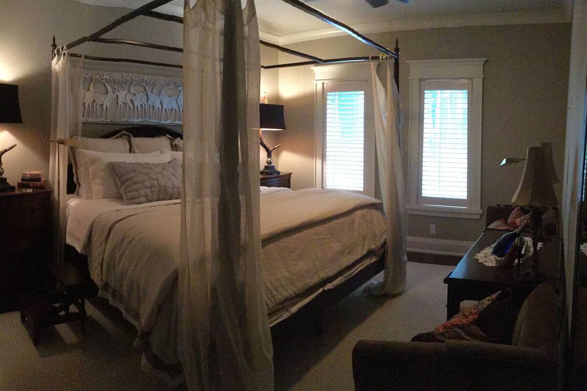 Una cama con dosel y cortinas, mesitas de noche con lámparas y una mesita auxiliar con lámpara.