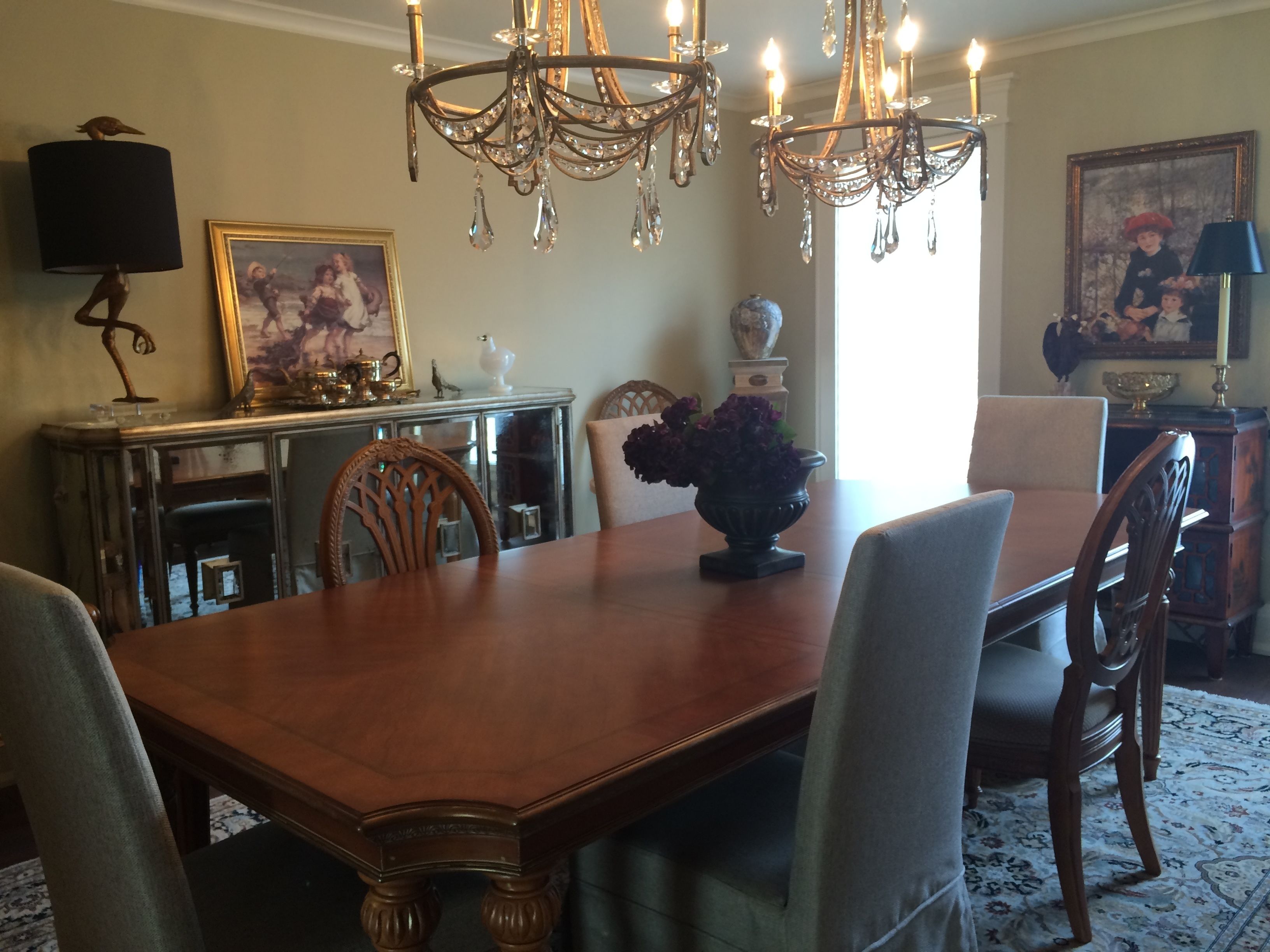 A dining room with a wooden table, chairs, a chandelier, and a vase with flowers.