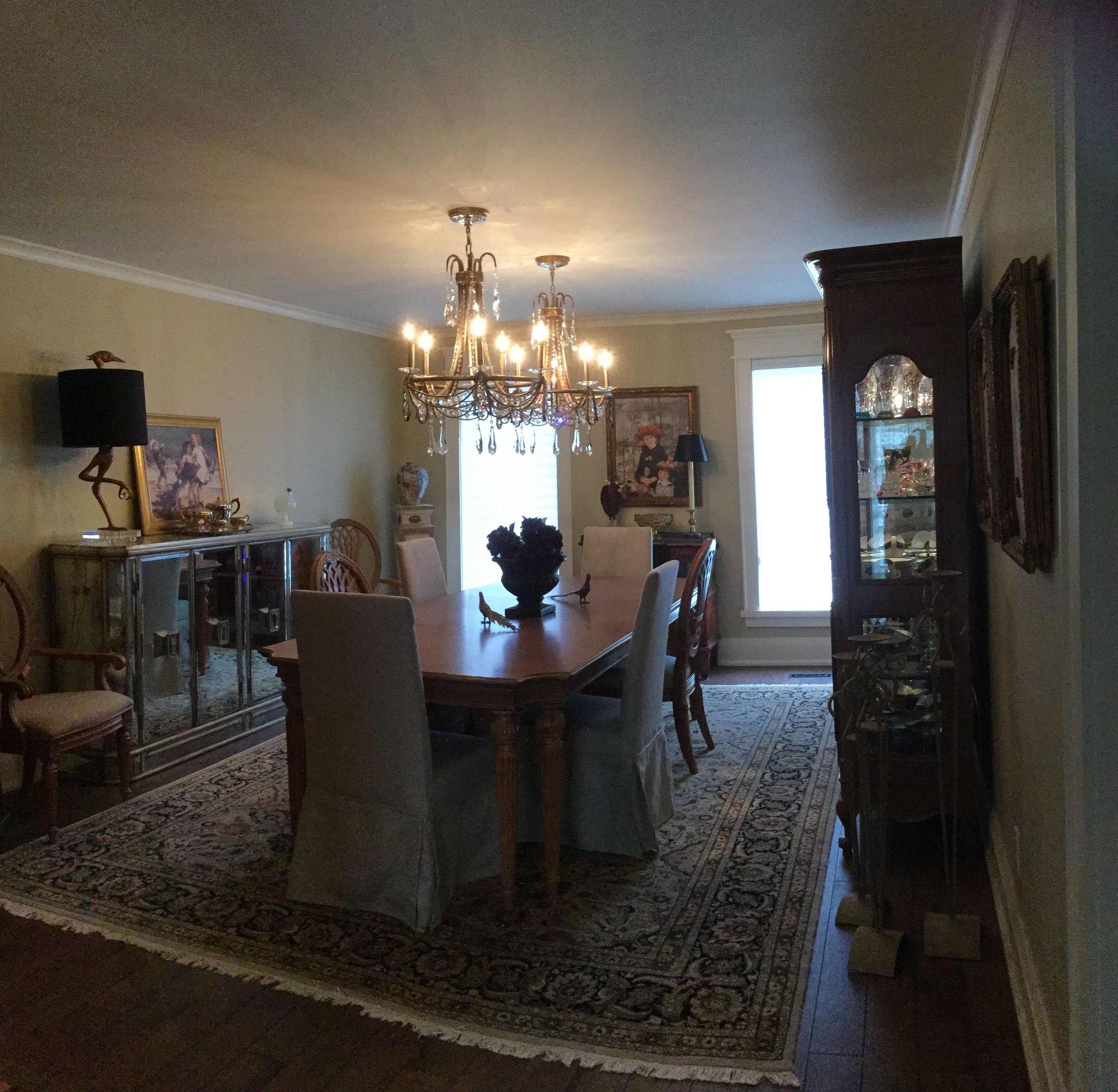 A dining room with a chandelier, wooden dining table, chairs, a rug, and a cabinet with glass doors.