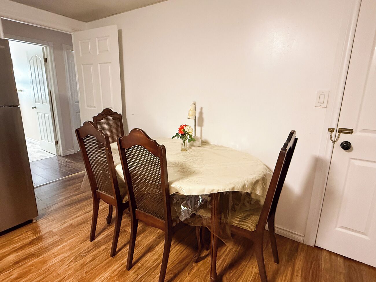 A dining area with a round table, four wooden chairs, and a vase with flowers.