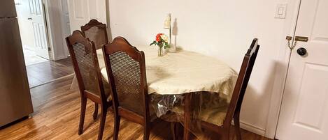 A dining area with a round table, four wooden chairs, and a vase with flowers.