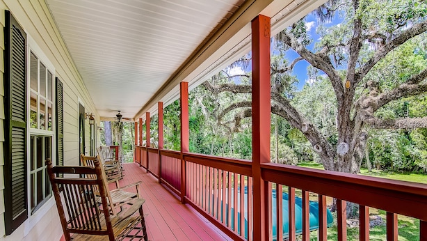 A covered porch with red railings, wooden rocking chairs, and a view of a backyard with a swimming pool and trees. - The Chassahowitzka Hotel (Homosassa)