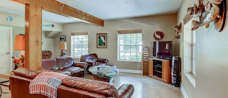 Un salon spacieux avec un canapé en cuir marron, un meuble de rangement en bois et un ventilateur de plafond.