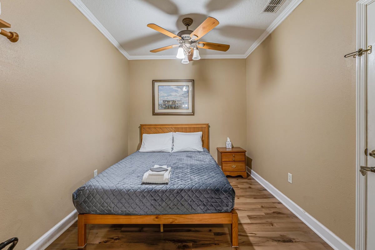 A bedroom with a wooden bed, a ceiling fan, a nightstand, and a framed picture on the wall.