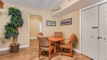 A dining area with a wooden table and four chairs, a potted plant, and two framed pictures on the wall.