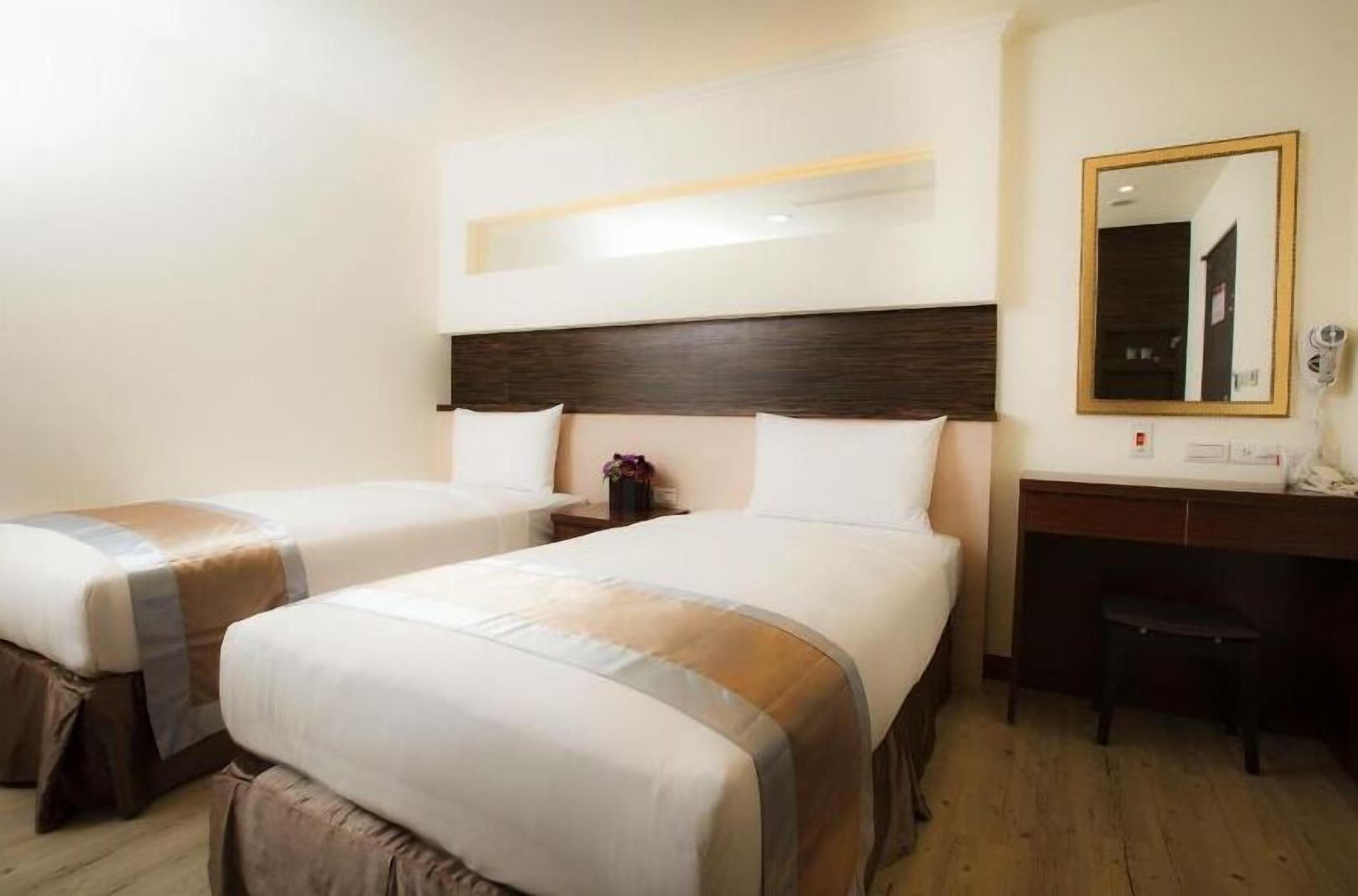 Ein Hotelzimmer mit zwei Betten, einem Schreibtisch, einem Stuhl und einem Spiegel.