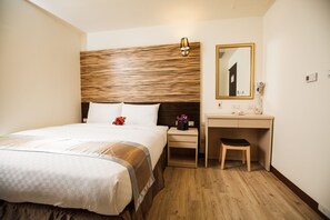 A hotel room with a large bed, a wooden headboard, a desk with a chair, a mirror, and a nightstand with a lamp. - Kaishen Hotel (Taitung)