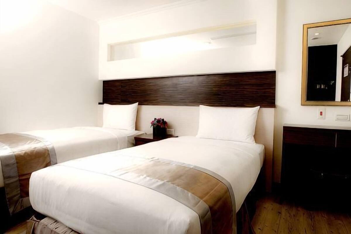 A hotel room with two beds, a wooden headboard, a nightstand, and a mirror.
