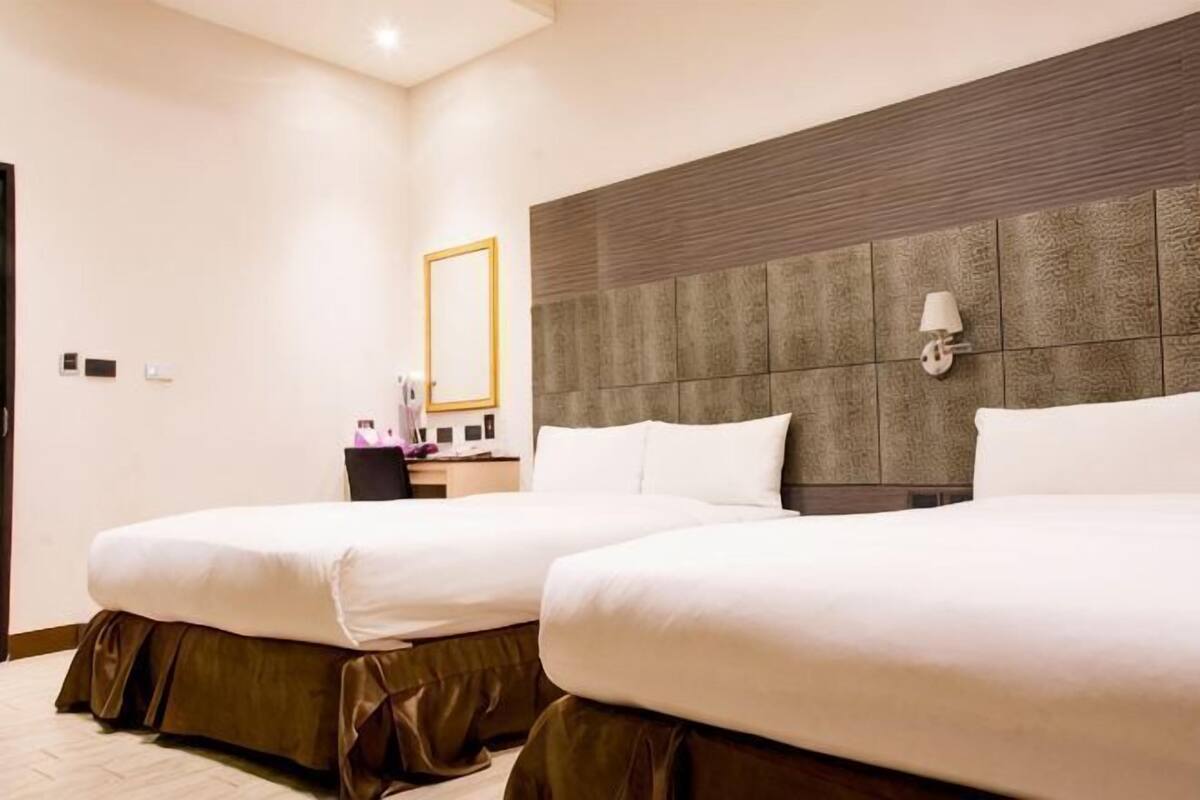 A hotel room with two beds, a large mirror, and a nightstand with a lamp.