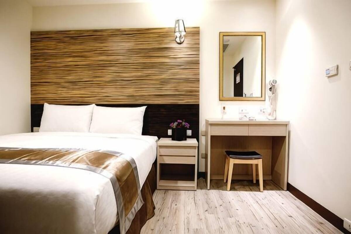 A hotel room with a bed, a desk, a chair, a mirror, and a nightstand.