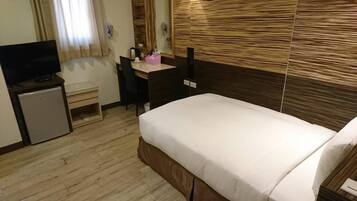 A hotel room with a bed, a desk with a chair, a television, and a small refrigerator.