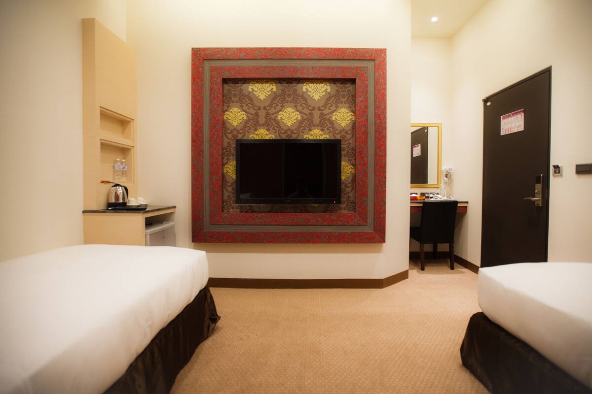 A hotel room with two beds, a desk, a mirror, and a wall-mounted television.
