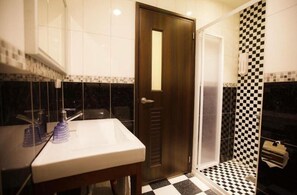 A bathroom with a white sink, a wooden door, and a checkered shower area. - Kaishen Hotel (Taitung)