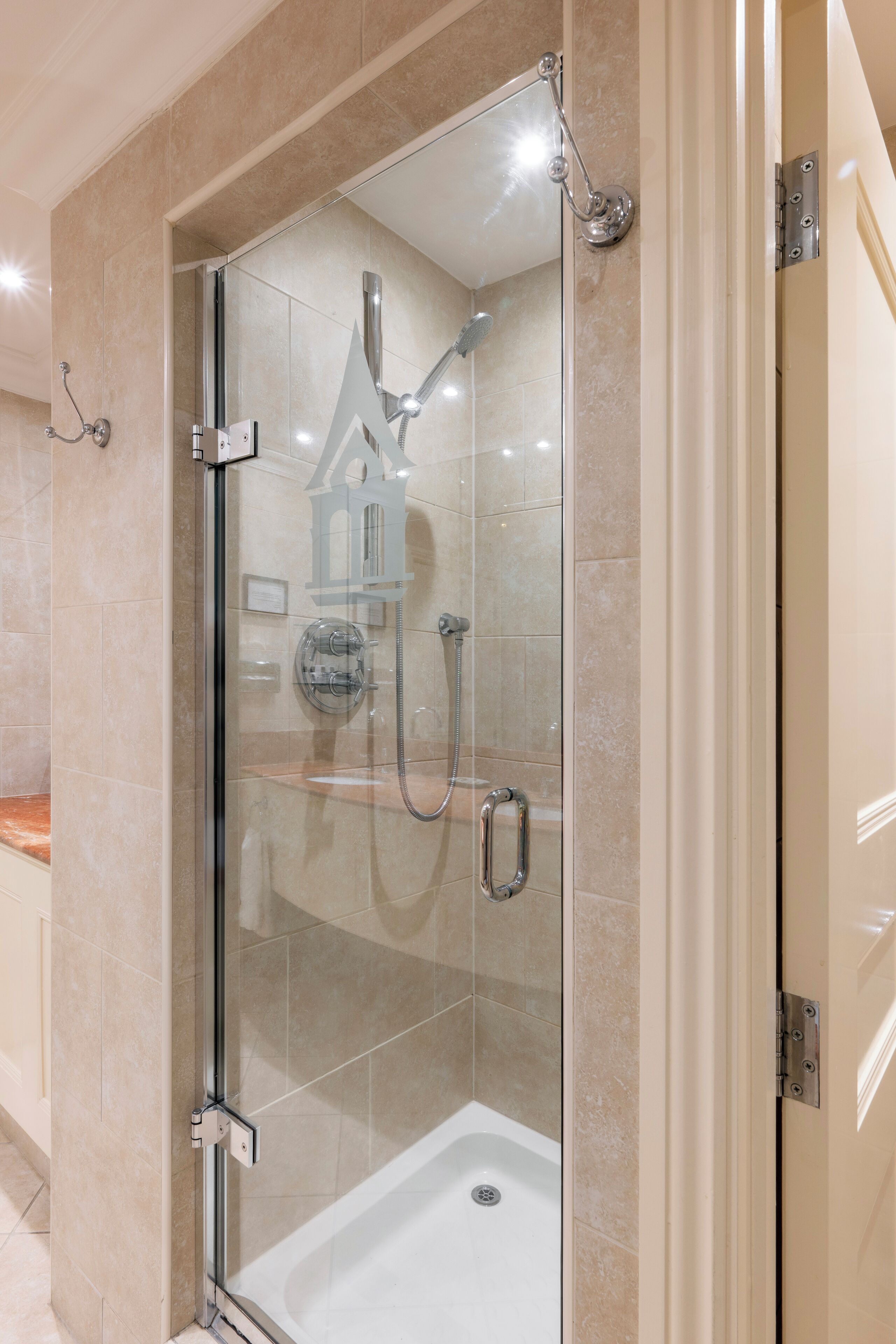 A glass-enclosed shower stall with a handheld showerhead and a handheld faucet.