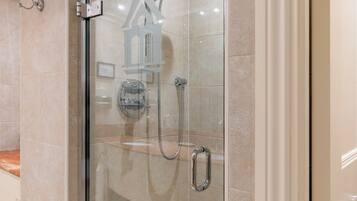 A glass-enclosed shower stall with a handheld showerhead and a handheld faucet.