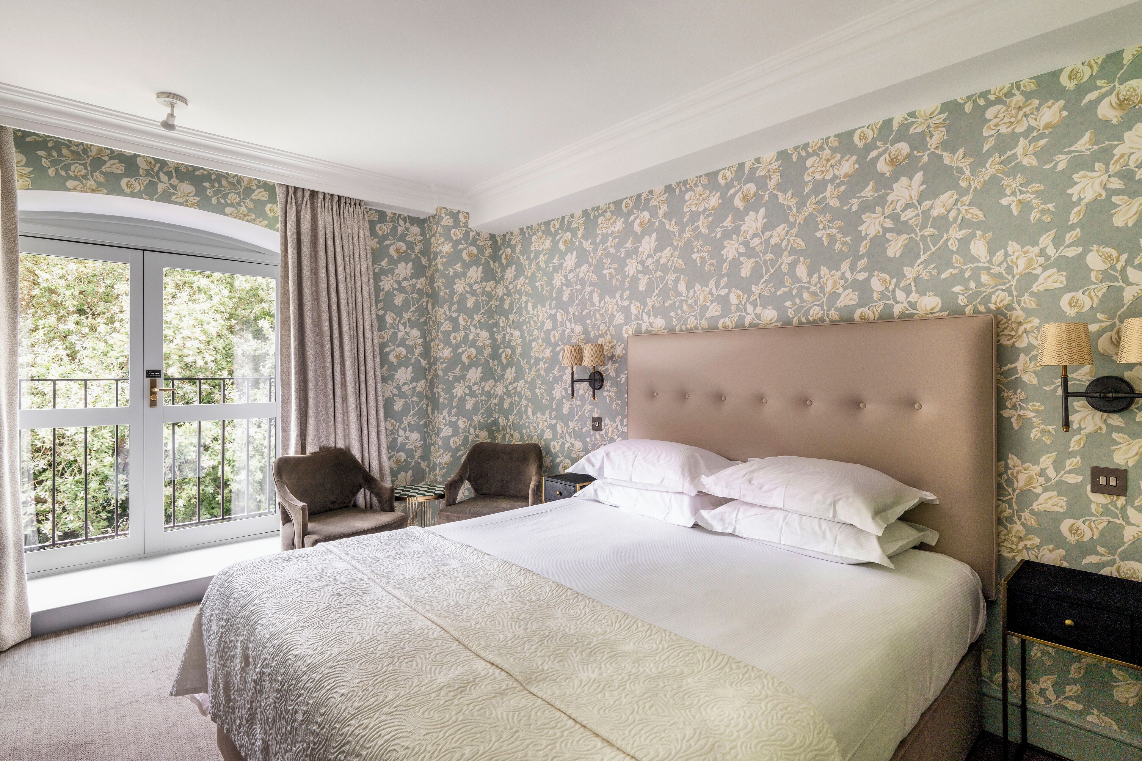 A bedroom with a large bed, two chairs, a nightstand, and a window with curtains.