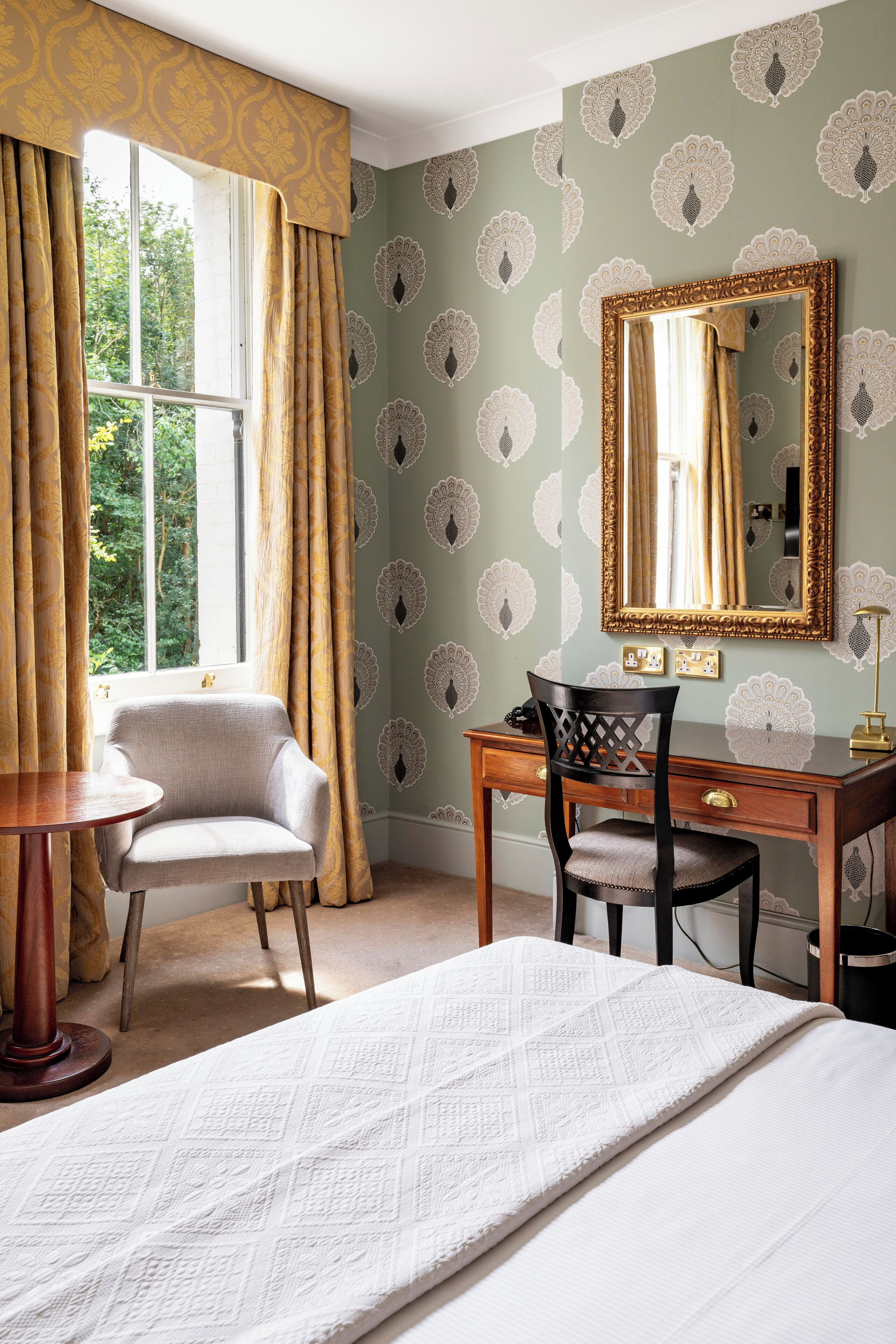 A room with a bed, a desk, a chair, a table, and a window with curtains.
