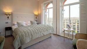 Une chambre à coucher avec un grand lit, deux lampes de chevet, une petite table et une vue sur un balcon doté d’une balustrade.