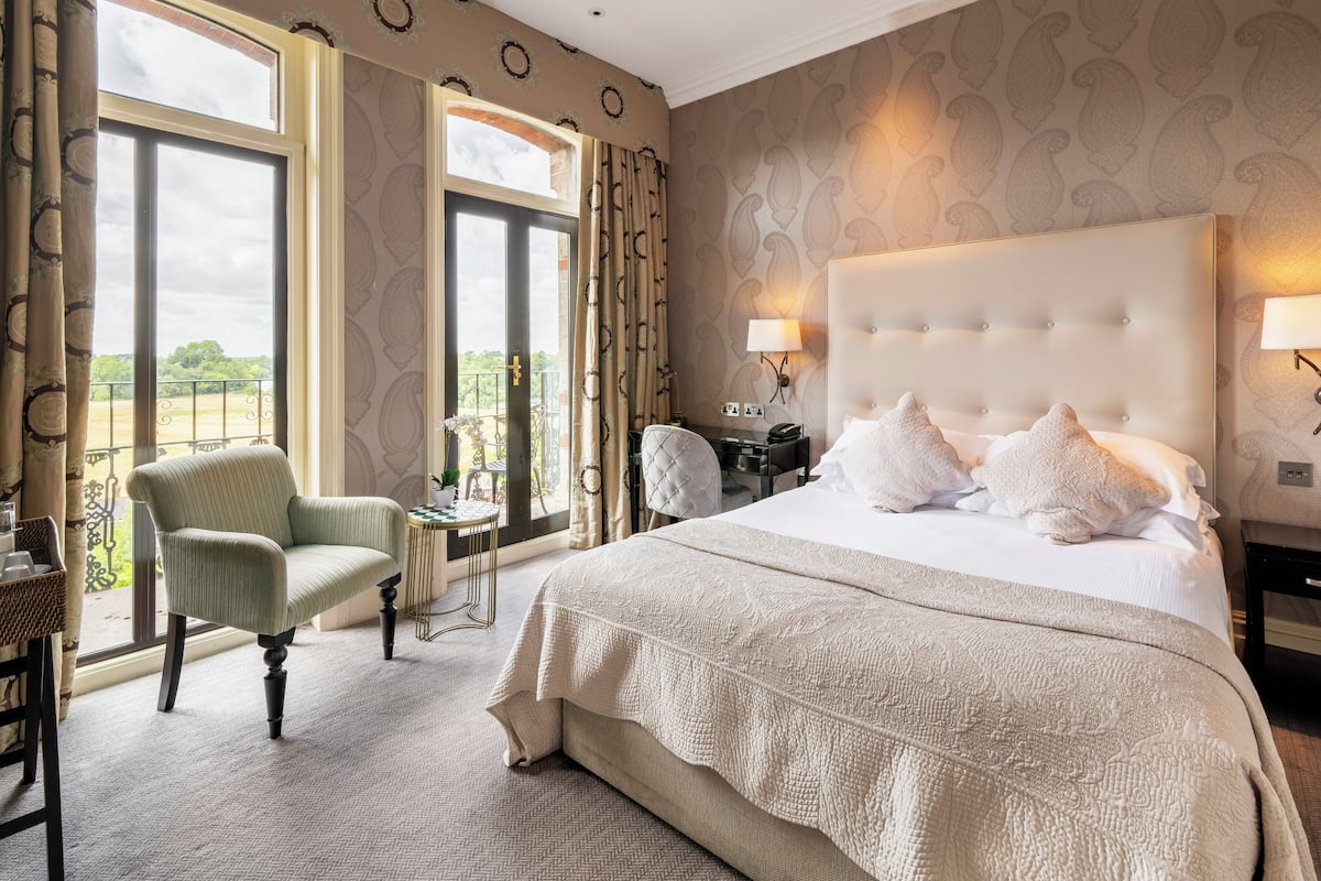 A spacious bedroom with a large bed, a sitting chair, and a view of the outdoors through a large window.