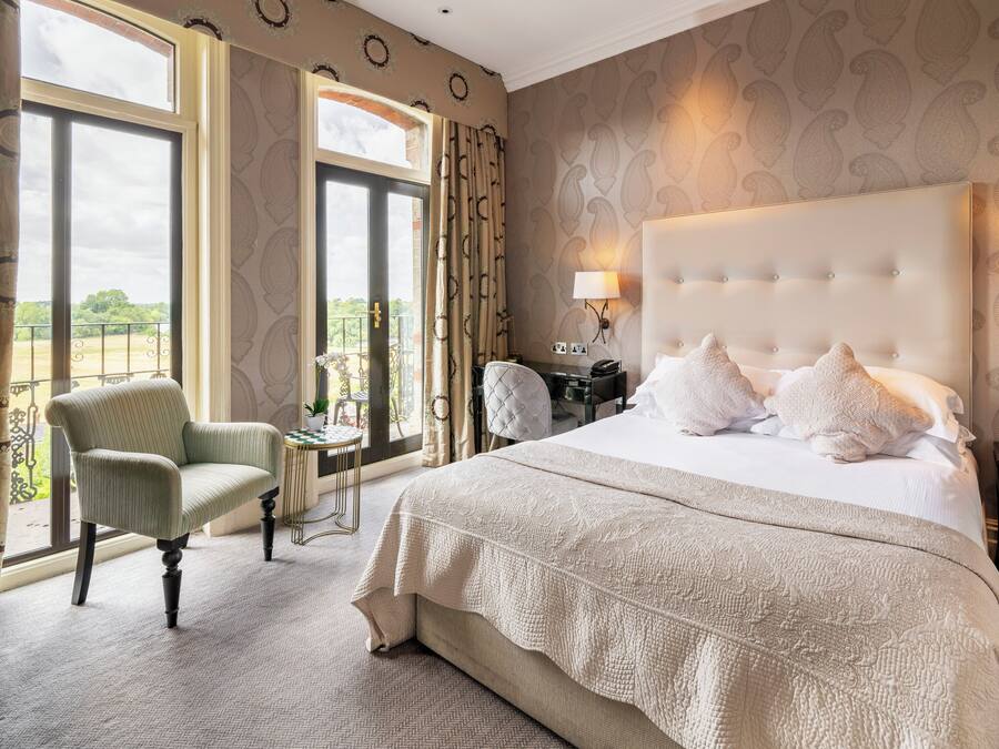 A spacious bedroom with a large bed, a sitting chair, and a view of the outdoors through a large window.