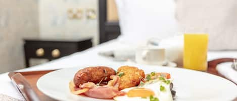 En morgenmadstallerken med pølser, spejlæg og en kartoffelpandekage på et hotelbord.