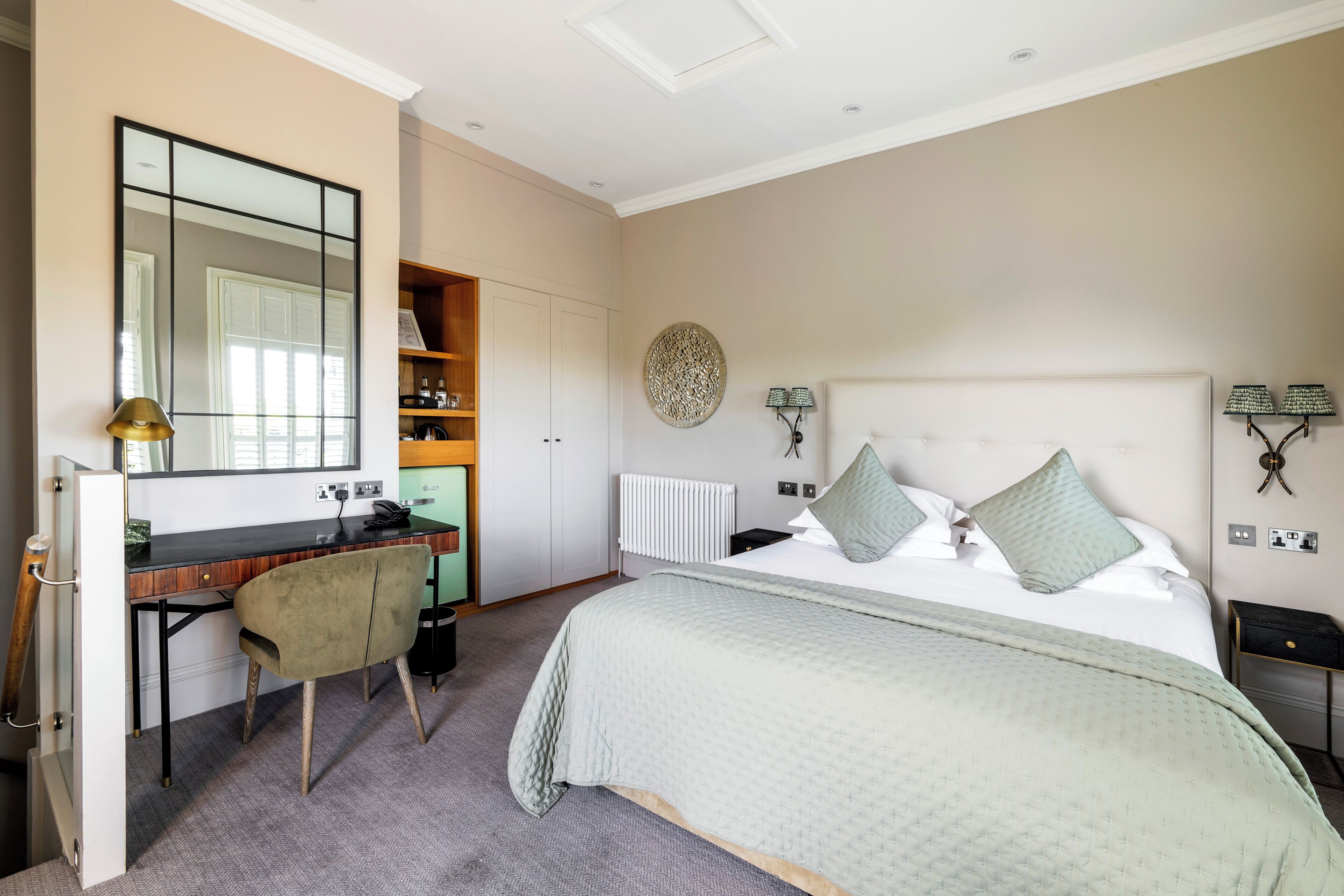 A bedroom with a bed, a desk, and a chair. There is a wardrobe, a radiator, and a wall-mounted lamp.