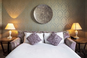 A neatly made bed with two pillows, two bedside tables with lamps, and a round wall decoration. - The Petersham (Richmond)
