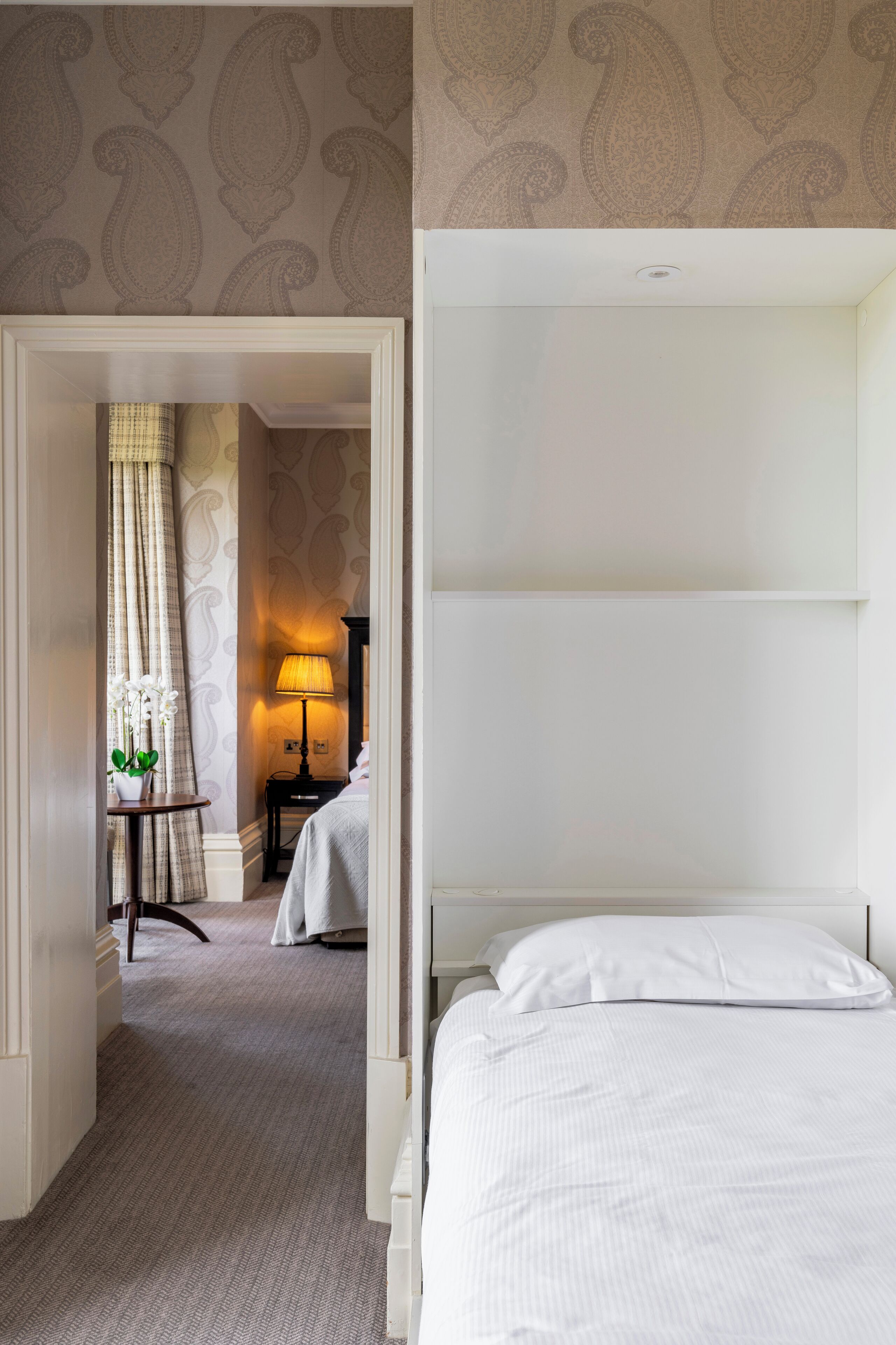 A hotel room with a bed, a desk with a lamp, and a chair.