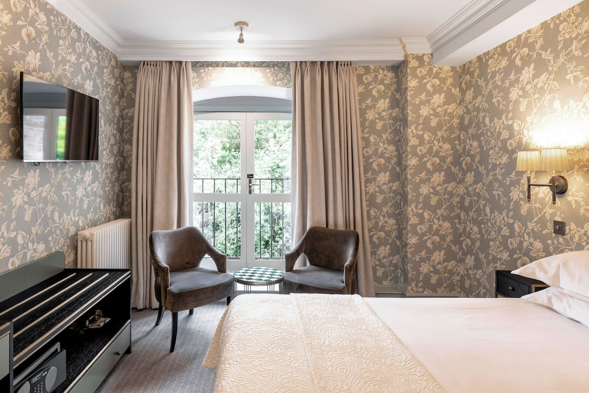 A hotel room with a bed, two armchairs, a small table, a TV, and a window with curtains.