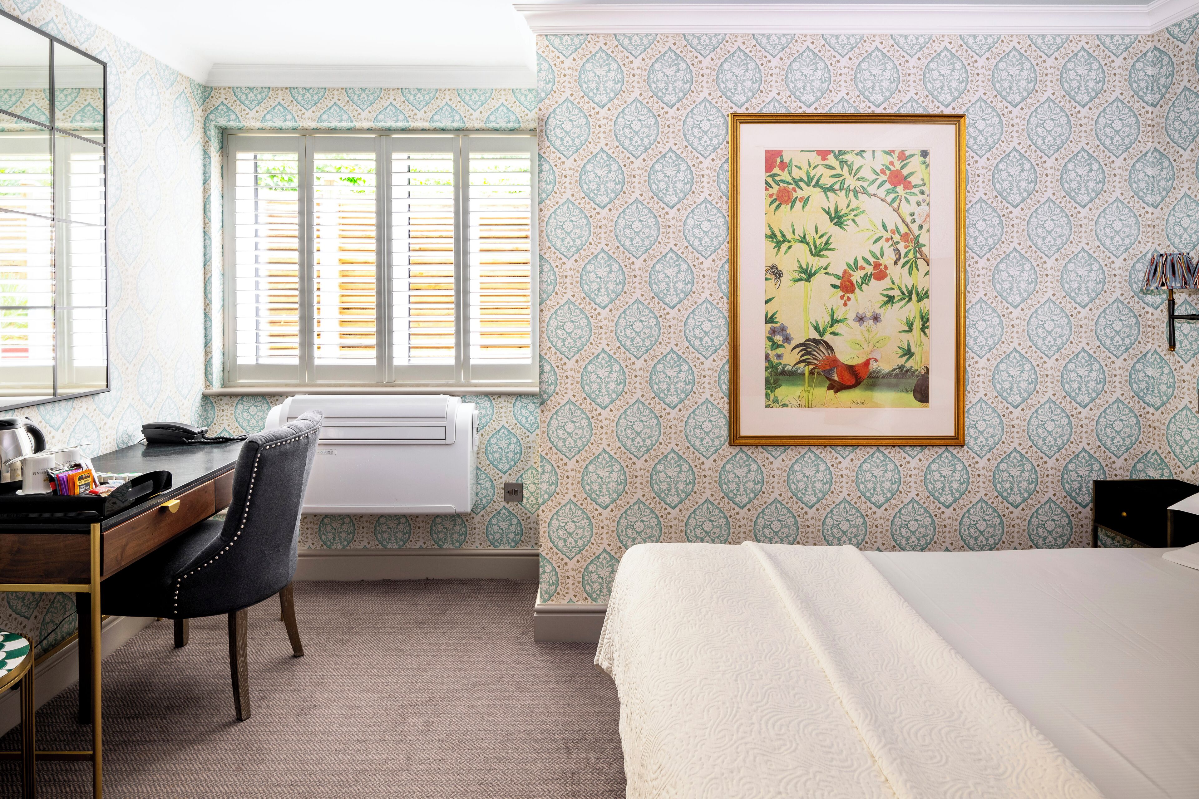 A hotel room with a bed, desk, chair, and a large framed picture on the wall.