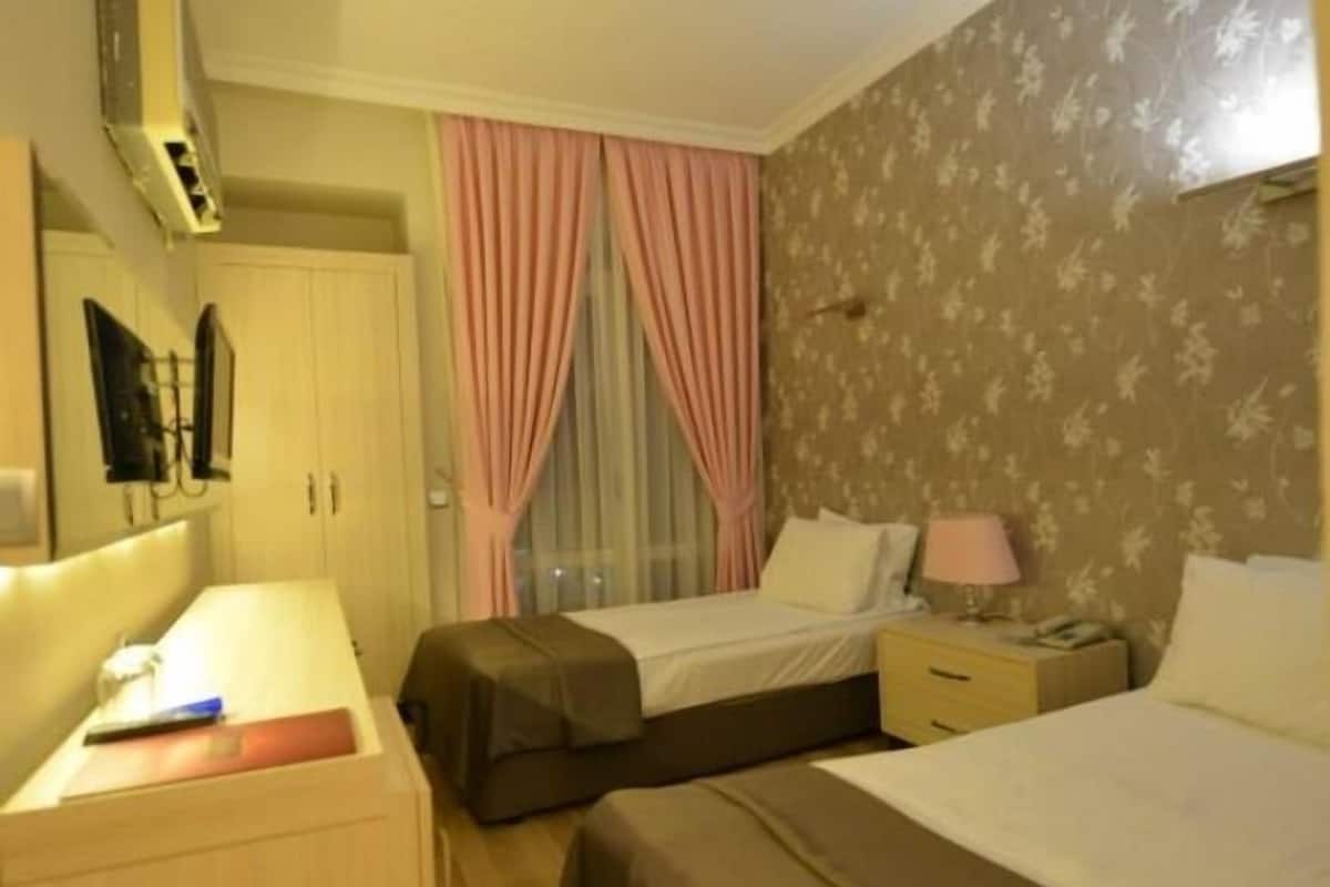 A hotel room with two beds, a desk, a wardrobe, and a window with curtains.
