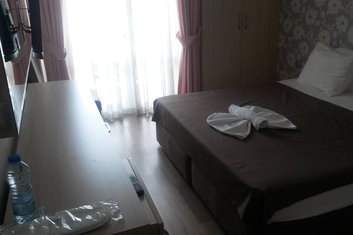 A hotel room with a bed, a desk, a water bottle, and a remote control.