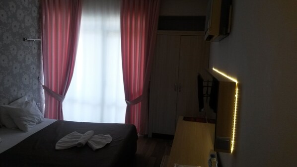 A hotel room with a bed, a window with curtains, a bedside table, and a mirror with lights.