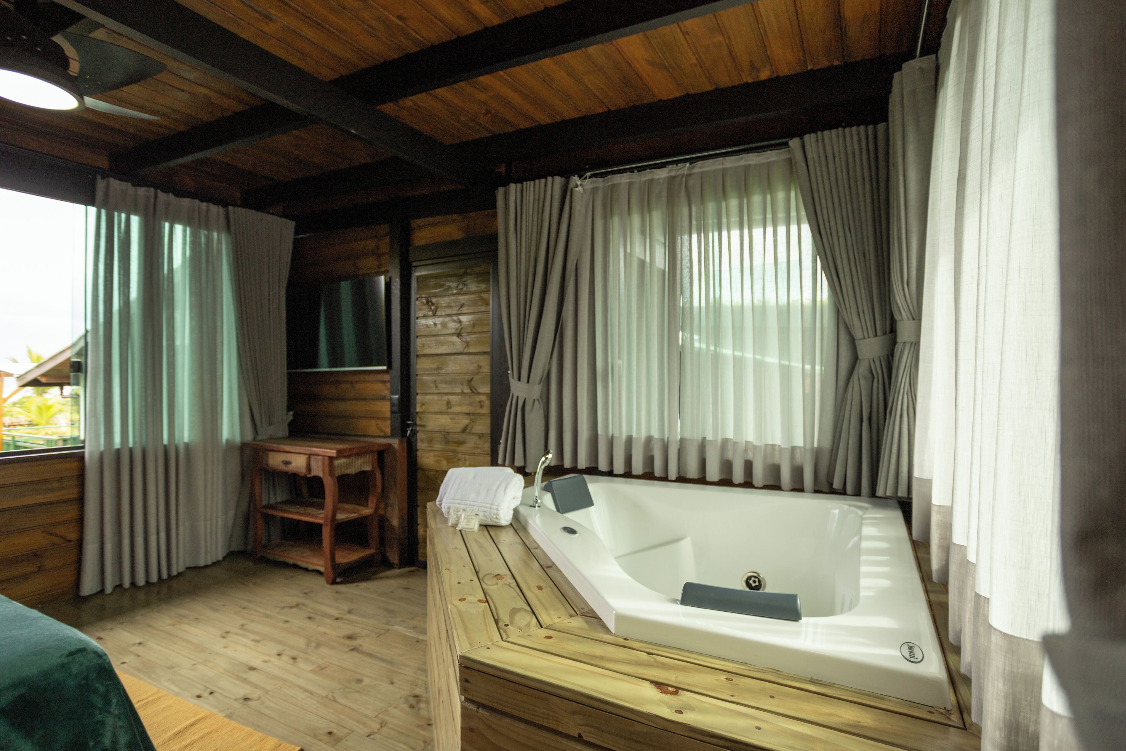 A wooden cabin with a wooden floor, a wooden bench, a white bathtub, and a window with curtains.