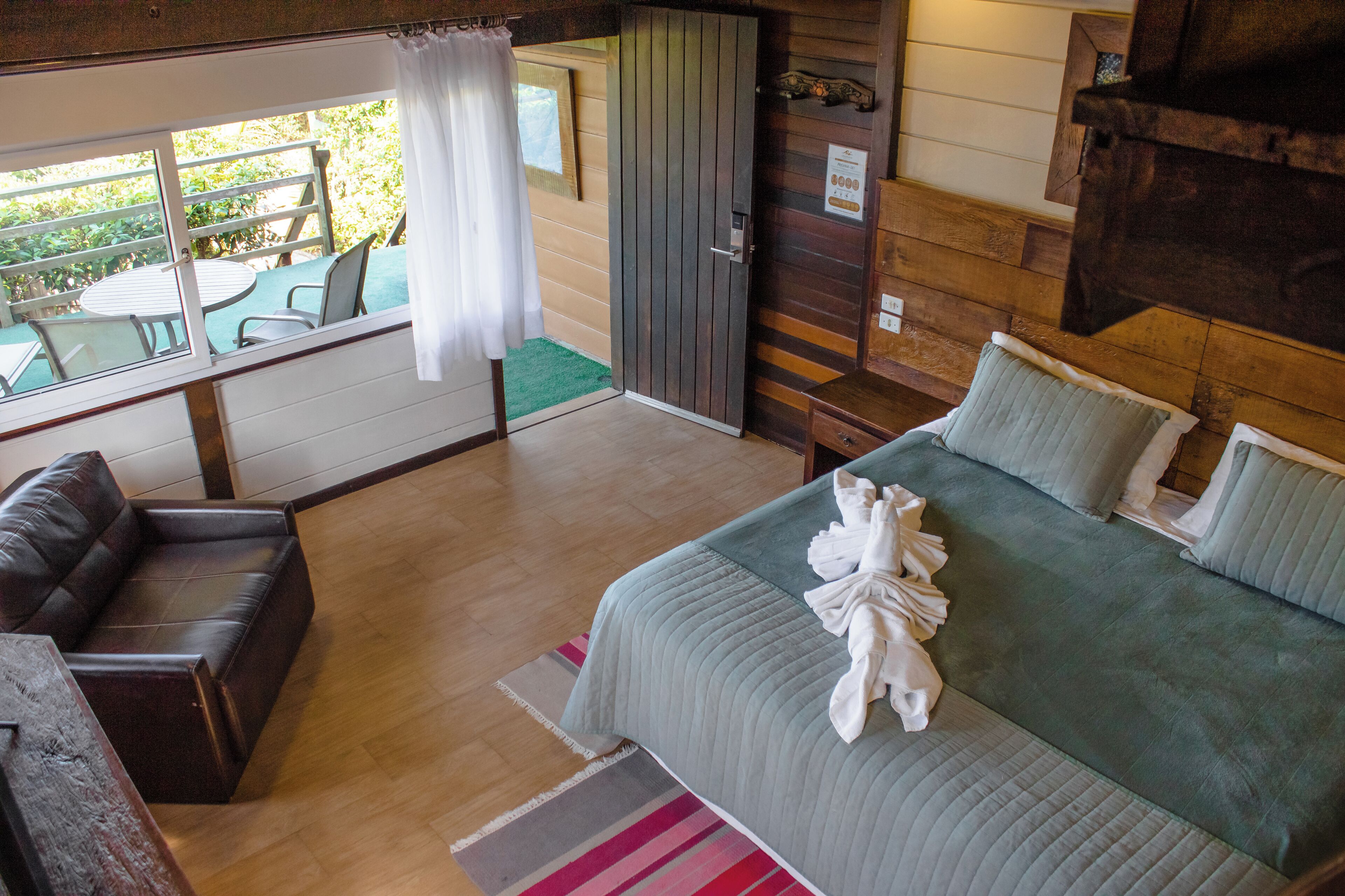 Ein Schlafzimmer mit einem Bett, einem Holzschrank, einer Sitzecke mit Tisch und Stühlen sowie Blick ins Freie.