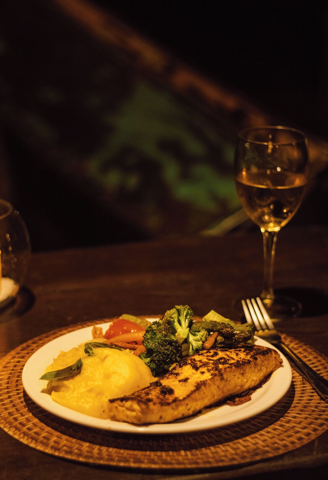 A plate of food with a glass of white wine on a table.