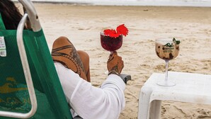 A person relaxing on a beach chair with a drink on a table. - Grajagan Surf Resort (Paranaguá)