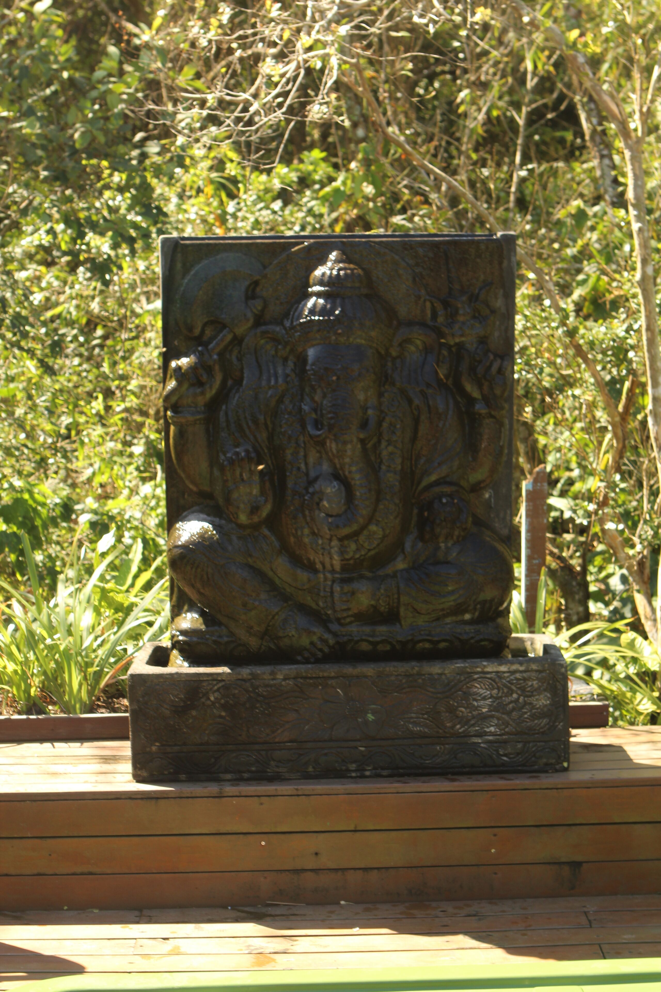 Una estatua de bronce de una deidad con forma de elefante sobre una plataforma de madera.