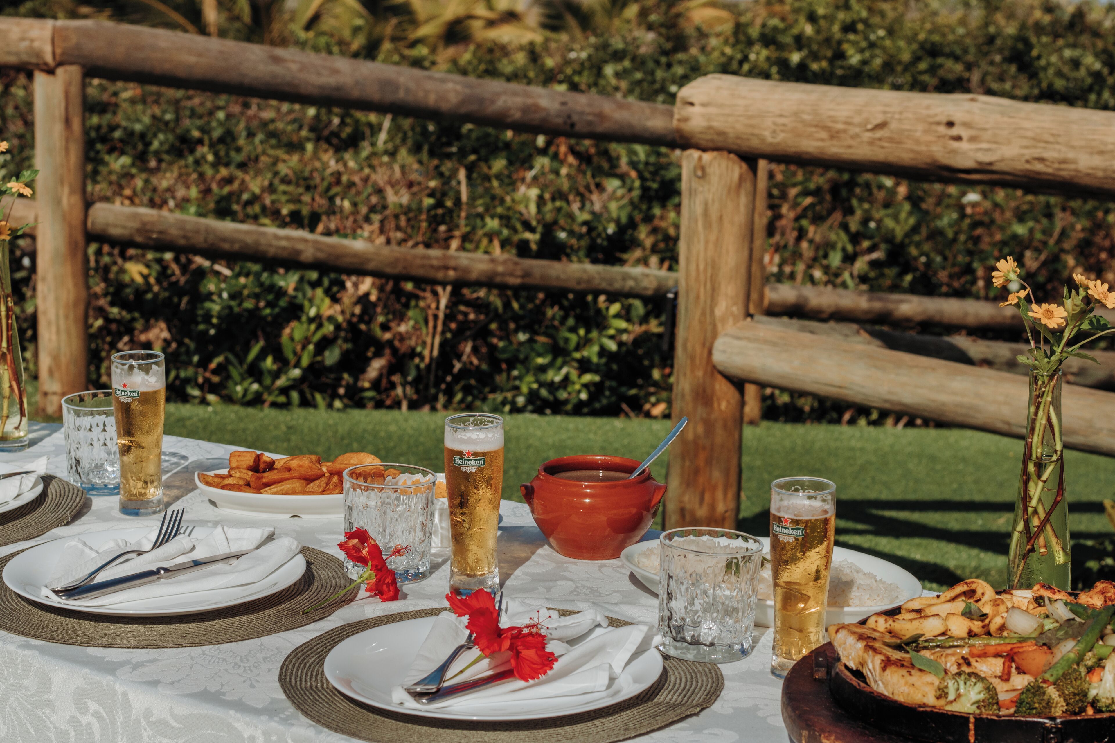 Une table dressée à l’extérieur, avec des assiettes de nourriture, des verres de bière et un bol de soupe.