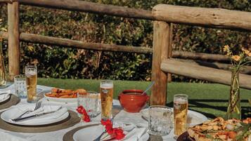 Une table dressée à l’extérieur, avec des assiettes de nourriture, des verres de bière et un bol de soupe.